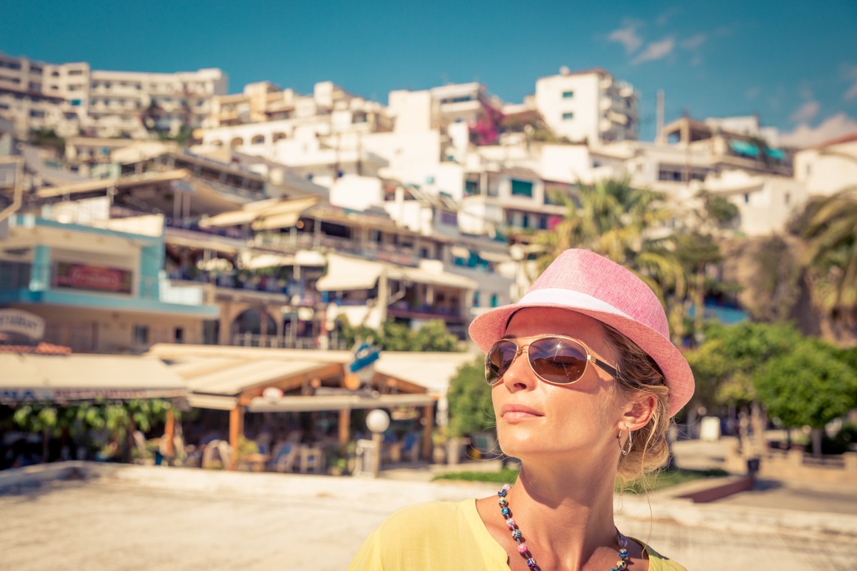 recorte de turista con sombrero rosa y gafas de sol con fondo pueblecito desenfocado